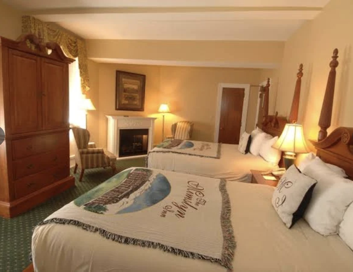 A warmly lit historic guest room with antiques, a fireplace and mimslyn throws on twin beds